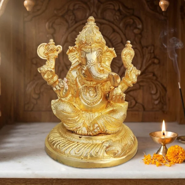 Brass Ganesh idol, 4.7 inch, on the marble shelf of a carved wooden home temple with a lit diya and marigolds