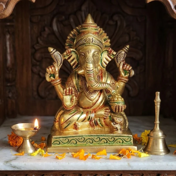 Brass Ganesh idol, 5.5 inch, on the marble shelf of a carved wooden home temple with a lit diya and bell