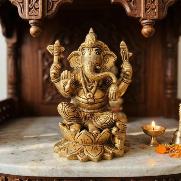 Brass Ganesh idol, 5 inch, on the marble shelf of a carved wooden home temple with a lit diya and bell