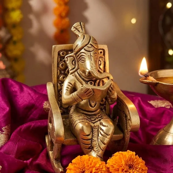 Brass reading Ganesh statue on magenta silk with a brass diya for Diwali