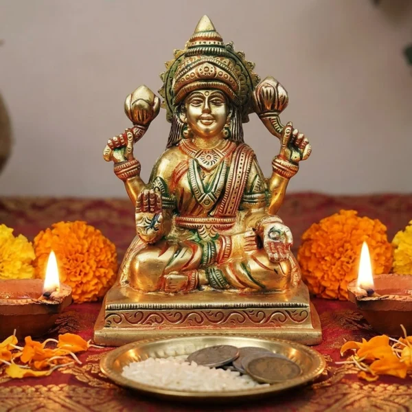 Brass Lakshmi idol, 5.5 inch, on a red and gold cloth with lit diyas, marigolds and a plate of rice and coins for Diwali puja