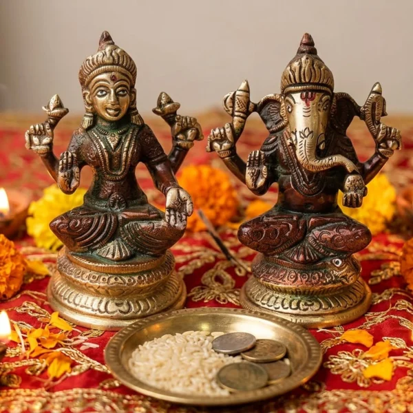 Brass Laxmi Ganesh pair on a red and gold cloth with lit diyas, marigolds and a plate of rice and coins for Diwali puja