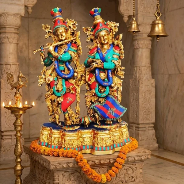 Brass Radha Krishna idol, 28 inch, with stone inlay on a carved stone pedestal in a temple hall with a lit deepak stand and marigold garland